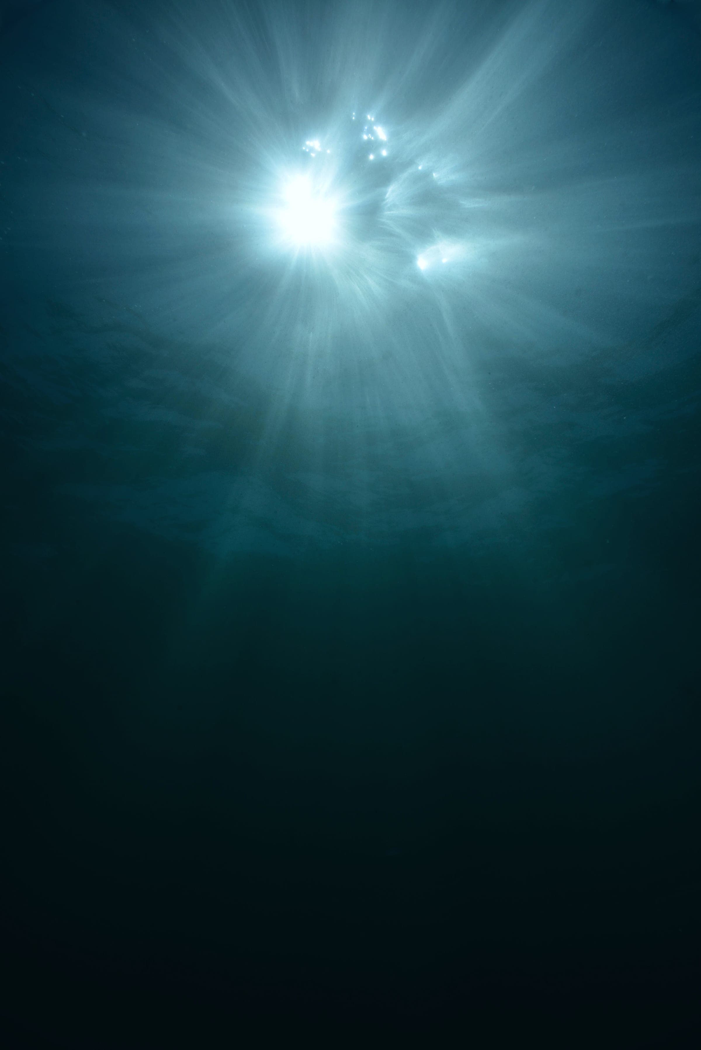 Sunlight streaming down through deep green-blue water, seen from below the surface